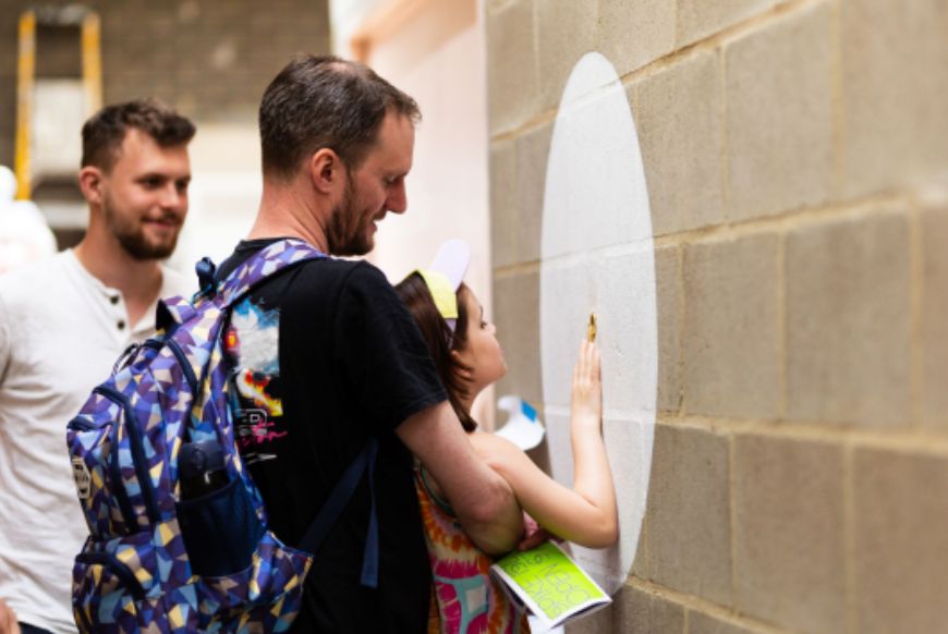 a man holding up a child to touch the wall, another man behind them